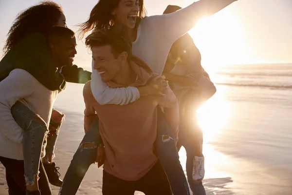 Grupp Vänner Med Piggyback Race Vintern Beach Tillsammans — Stockfoto