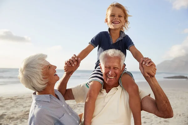 祖父母が孫を乗せてビーチに沿って散歩に肩 — ストック写真