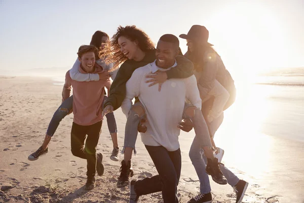 Grupp Vänner Med Piggyback Race Vintern Beach Tillsammans — Stockfoto