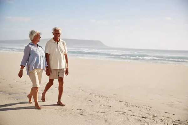 シニア引退カップル一緒に手をつないでビーチを歩いて — ストック写真