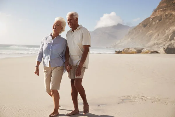 シニア引退カップル一緒に手をつないでビーチを歩いて — ストック写真