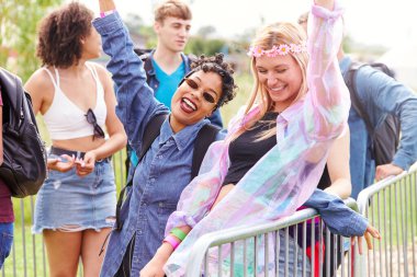 Portrait Of Female Friends Waiting Behind Barrier At Entrance To Music Festival Site clipart