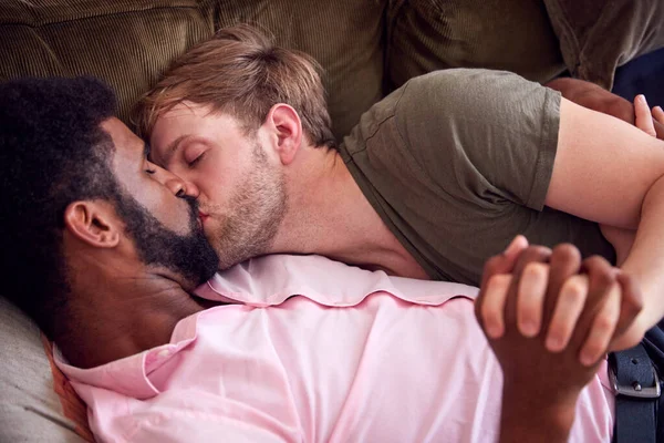 愛する男性ゲイカップルリラックスします自宅でソファに横たわっ抱擁とキス — ストック写真