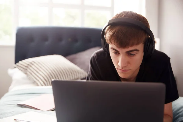 Erkek Kolej Öğrencisi Kulaklık Takıyor Laptopta Çalışırken Yatakta Uzanıyor — Stok fotoğraf