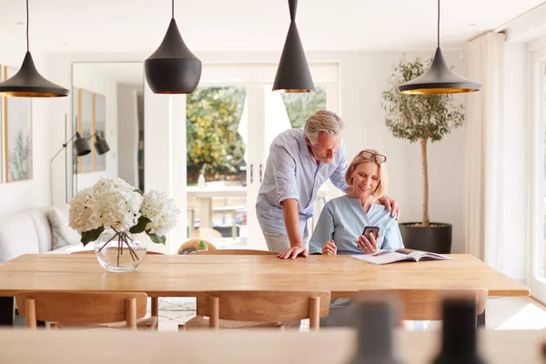 Oudere Paar Ontspannen Met Magazine Thuis Zoek Naar Mobiele Telefoon — Stockfoto