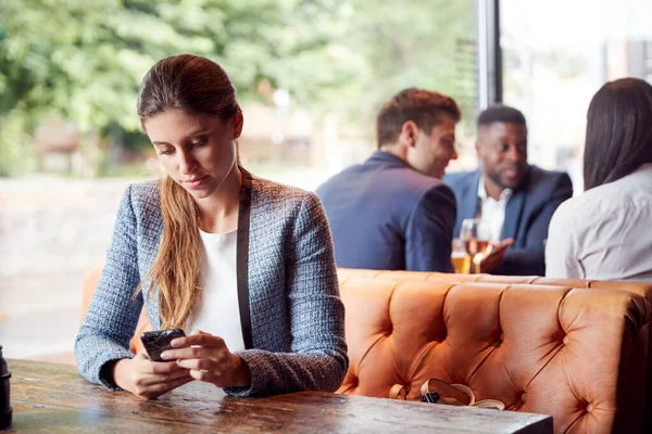 Geschäftsfrau Sitzt Bar Und Checkt Mobiltelefone Während Sich Kollegen Hintergrund — Stockfoto
