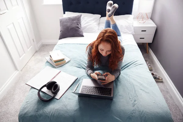 Patrząc Dół Studentkę College Leżącą Łóżku Pracującą Laptopie Korzystającą Telefonu — Zdjęcie stockowe