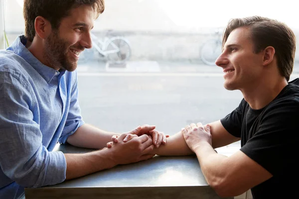 Amante macho gay pareja sentado en mesa en café tienda celebración h —  Fotos de Stock