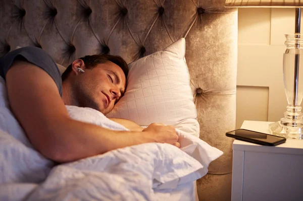 Hombre Durmiendo Cama Con Auriculares Inalámbricos Conectados Teléfono Móvil Mesita —  Fotos de Stock