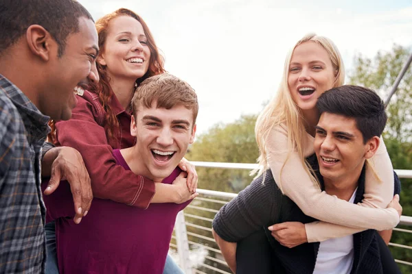 Studenti Přátelé Muži Dává Ženám Piggyback Vyjížďky Přes City Bridge — Stock fotografie