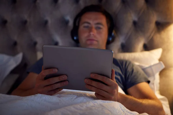 Muž Bezdrátovými Sluchátky Ležící Posteli Sledující Digitální Tablet Před Spaním — Stock fotografie