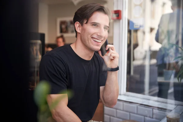 Young Man In Coffee Shop Talking On Mobile Phone Viewed Through — Stock Photo, Image