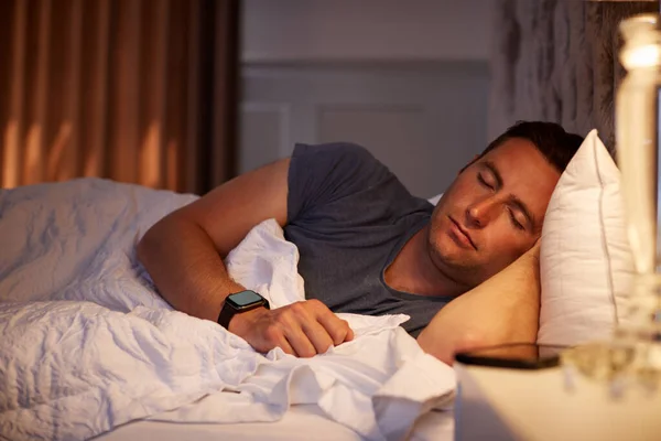 Homem Dormindo Cama Vestindo Relógio Inteligente Iluminado Pela Lâmpada Cabeceira — Fotografia de Stock