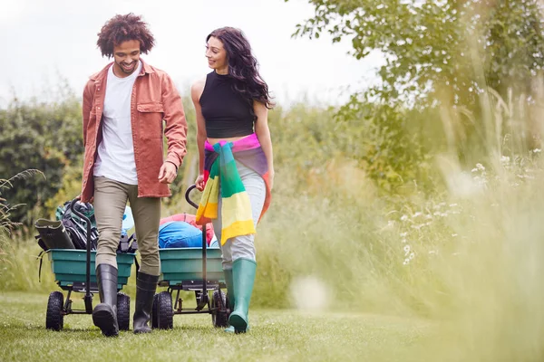 Junges Paar Zieht Mit Campingausrüstung Gefüllten Einkaufswagen Durch Feld Zum — Stockfoto
