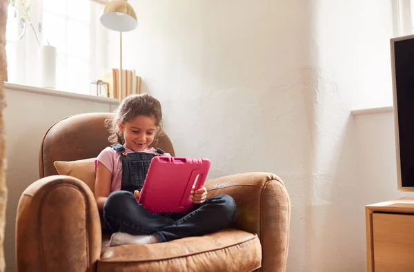 女の子は自宅でデジタルタブレットで遊んでアームチェアに座って — ストック写真