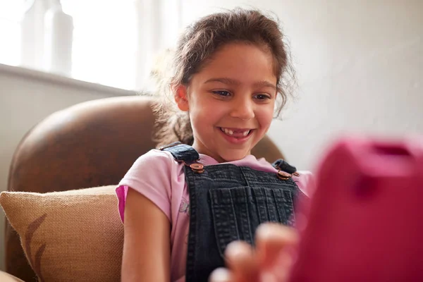 女の子は自宅でデジタルタブレットで遊んでアームチェアに座って — ストック写真