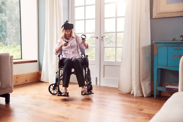 ゲームコントローラーを装着したバーチャルリアリティヘッドセットを装着した自宅で車椅子の熟女 — ストック写真