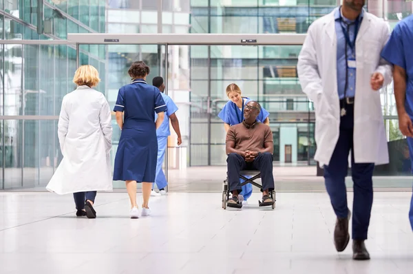 通过现代医院大楼前厅 女护士穿着洗车将病人推上轮椅 — 图库照片