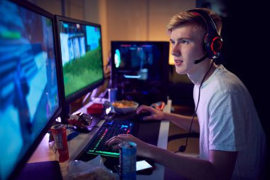 Teenage Boy Wearing Headset Gaming At Home Using Dual Computer Screens clipart