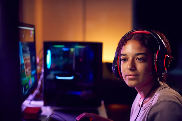 Teenage Girl Wearing Headset Gaming At Home Using Dual Computer Screens