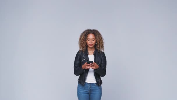 若い女性は 携帯電話でテキストメッセージを送信レザージャケットを身に着けている白いスタジオの背景に対して検索 スローモーションで撮影 — ストック動画