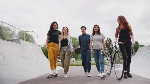 スケートボードと自転車で街のスケートパークを一緒に歩く女性の友人のグループ スローモーションで撮影 — ストック動画