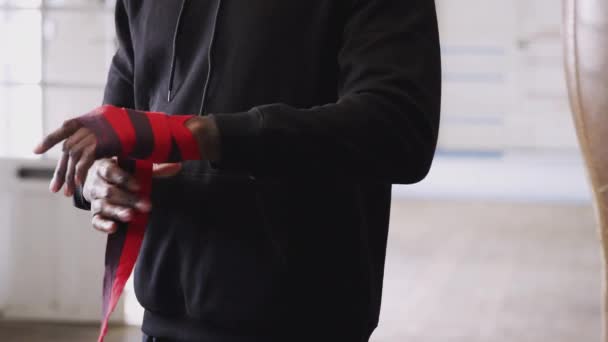 ジムでの男性ボクサーのクローズアップは 古いスタイルの革パンチバッグの横に手に保護ラップを置く スローモーションで撮影 — ストック動画