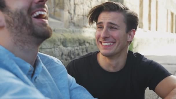 Erkek Eşcinsel Çift Şehir Binasının Önünde Oturmuş Birlikte Gülüyorlar Ağır — Stok video