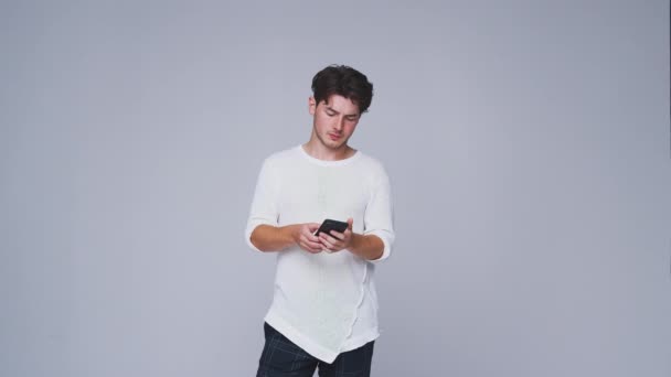 Young Man Sending Text Message Mobile Phone Looks White Studio — Stock Video