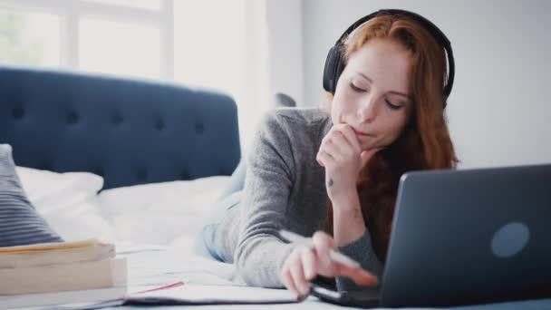 Γυναίκα Φοιτήτρια Ξαπλωμένη Στο Κρεβάτι Φορώντας Ακουστικά Και Δουλεύοντας Laptop — Αρχείο Βίντεο