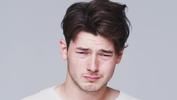 不快乐的年轻人的头和肩膀照在镜头前 面对着白色的摄影棚背景 脸上带着忧郁的表情 慢镜头 — 图库视频影像