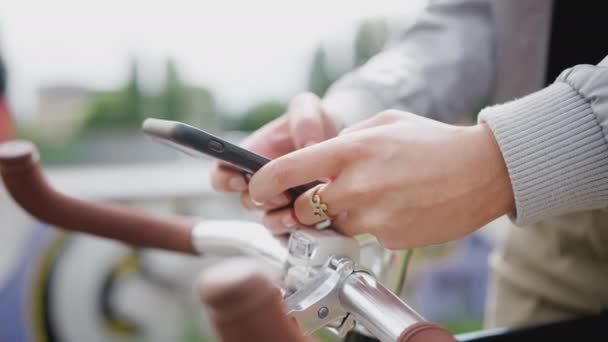 スケートパークでの女性の閉鎖自転車のハンドルバーに携帯電話を休ませ テキストメッセージを送信 スローモーションで撮影 — ストック動画