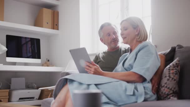 シニアカップル座ってソファに自宅で使用してデジタルタブレット一緒に 遅い動きで撮影 — ストック動画