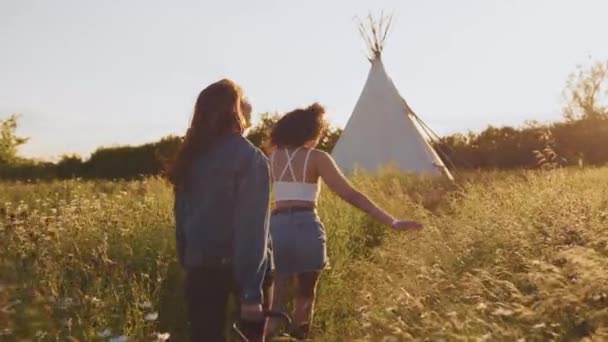 Visão Traseira Duas Amigas Caminhando Pelo Campo Direção Teepee Acampamento — Vídeo de Stock