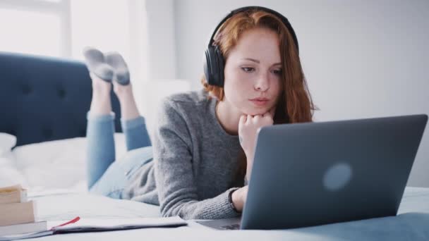 女大学生头戴耳机躺在床上 用手提电脑工作 动作缓慢 — 图库视频影像