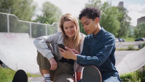 Twee Vrouwelijke Vrienden Kijken Naar Mobiele Telefoon Lachen Stad Skate — Stockvideo