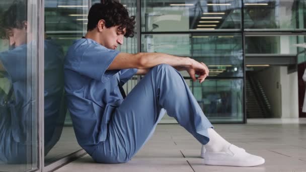 Tired Junior Doctor Wearing Scrubs Sitting Wall Modern Hospital Building — Stock Video