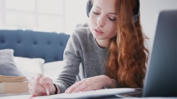 Estudiante Universitaria Acostada Cama Con Auriculares Trabajando Computadora Portátil Filmada — Vídeo de stock