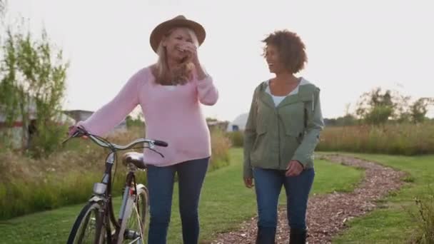 Two Mature Female Friends Walking Path Pushing Bike Yurt Campsite — Stock Video