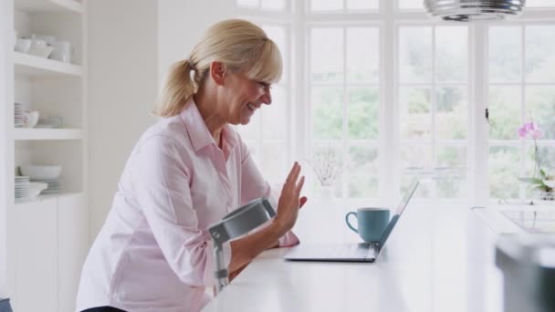 自宅でクラッチを使用しているシニア障害者の女性はキッチンカウンターでラップトップを使用してビデオ通話を持っています スローモーションで撮影 — ストック動画