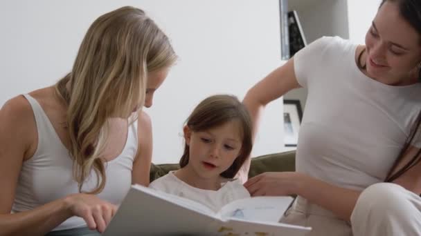 Samma Kön Kvinnliga Par Läser Bok Med Dotter Hemma Skjuten — Stockvideo