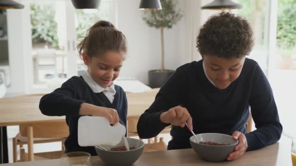 2人の子供が学校の制服を着てキッチンカウンターで不健康な朝食シリアルを食べる スローモーションで撮影 — ストック動画