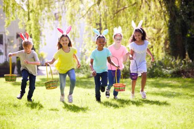 Group Of Children Wearing Bunny Ears Running To Pick Up Chocolate Egg On Easter Egg Hunt In Garden clipart