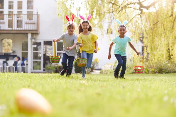 一群带着小兔子耳朵的孩子们在花园里跑着吃复活节彩蛋 — 图库照片