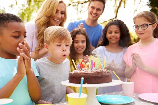 彼は自宅で庭で両親や友人のためのパーティーで誕生日を祝うように男の子はキャンドルを吹きます — ストック写真