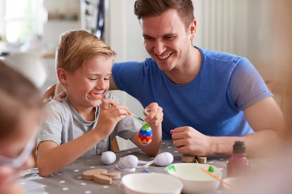 テーブルに座っている子供たちと父自宅でイースターのための卵を飾る — ストック写真