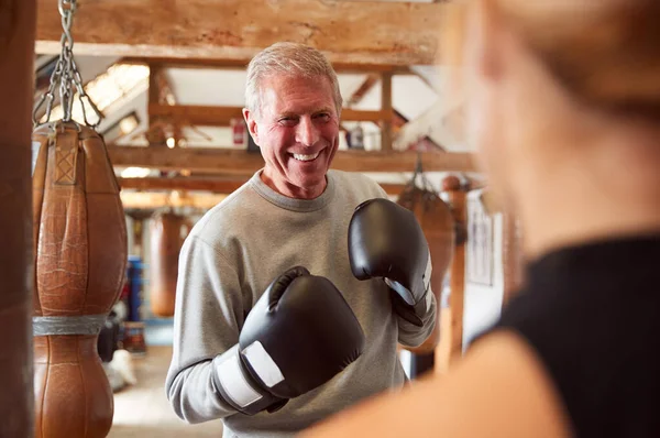 高级男子拳击手与年轻女子教练在健身房使用训练手套 — 图库照片