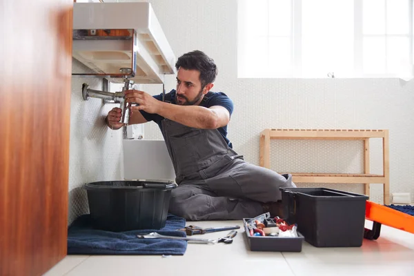 自宅のバスルームで漏れのシンクを修正するために働く男性配管工 — ストック写真