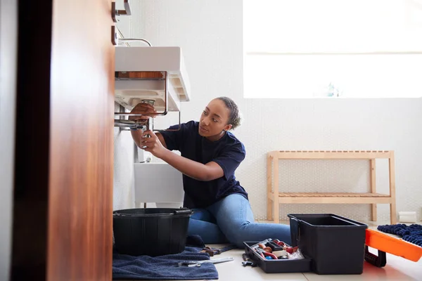 Female Plumber Working To Fix Leaking Sink In Home Bathroom