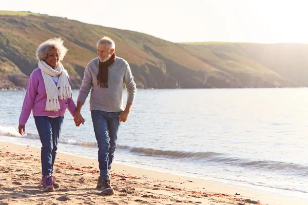 彼らは冬のビーチ休暇に海岸線に沿って歩くように引退したカップルを保持手を愛する — ストック写真